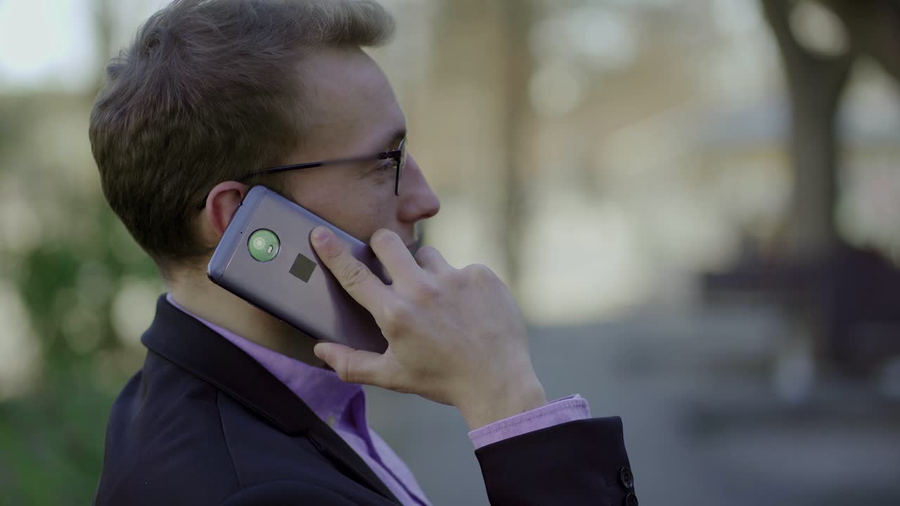 hombre de negocios sonriente con gafas hablando en el teléfono inteligente al aire libre