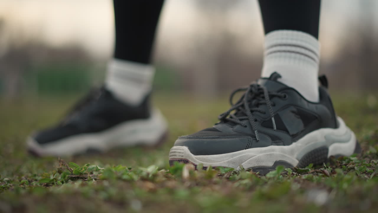 Closeup Of Black Sneakers On Grass, LowAngle Shot Showing Laced Chunky Trainers, White Crew Socks, Slight Dirt On Sole, Ambient Overcast Light, Quiet Park Setting, Runner Preparing For Interval