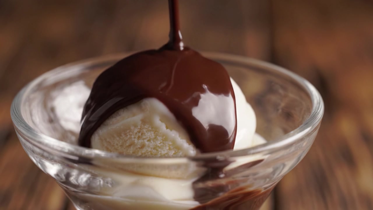 Decadente salsa al cioccolato versata su cremoso gelato alla vaniglia in un'elegante ciotola di vetro – Una delizia tentatrice per gli amanti dei dessert.