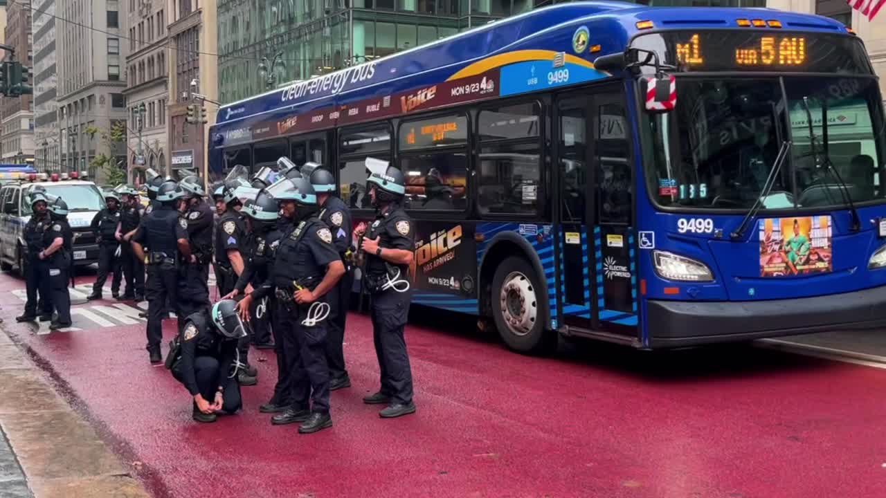 Police officers and pedestrians on a busy New York City street with a bus