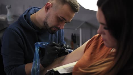 portrait of a tattoo artist demonstrates the process of getting colour tattoo. modern tattoo parlor. bearded tattoo artist and a female client on foreground in a beauty salon