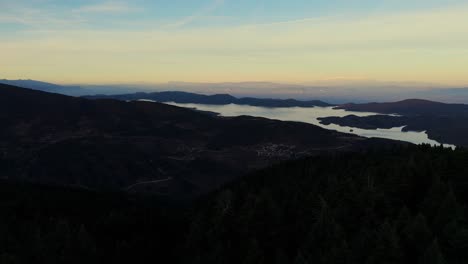 drone flies above dark conifer tree silhouetttes to reveal scenic lake kerkini at sunset