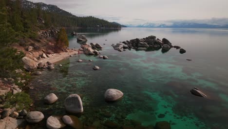swimming cold plunge dive sunny winter day sand harbor secret beach south lake tahoe aerial drone california shoreline large boulder rocks crystal clear glassy turquoise fresh water static shot