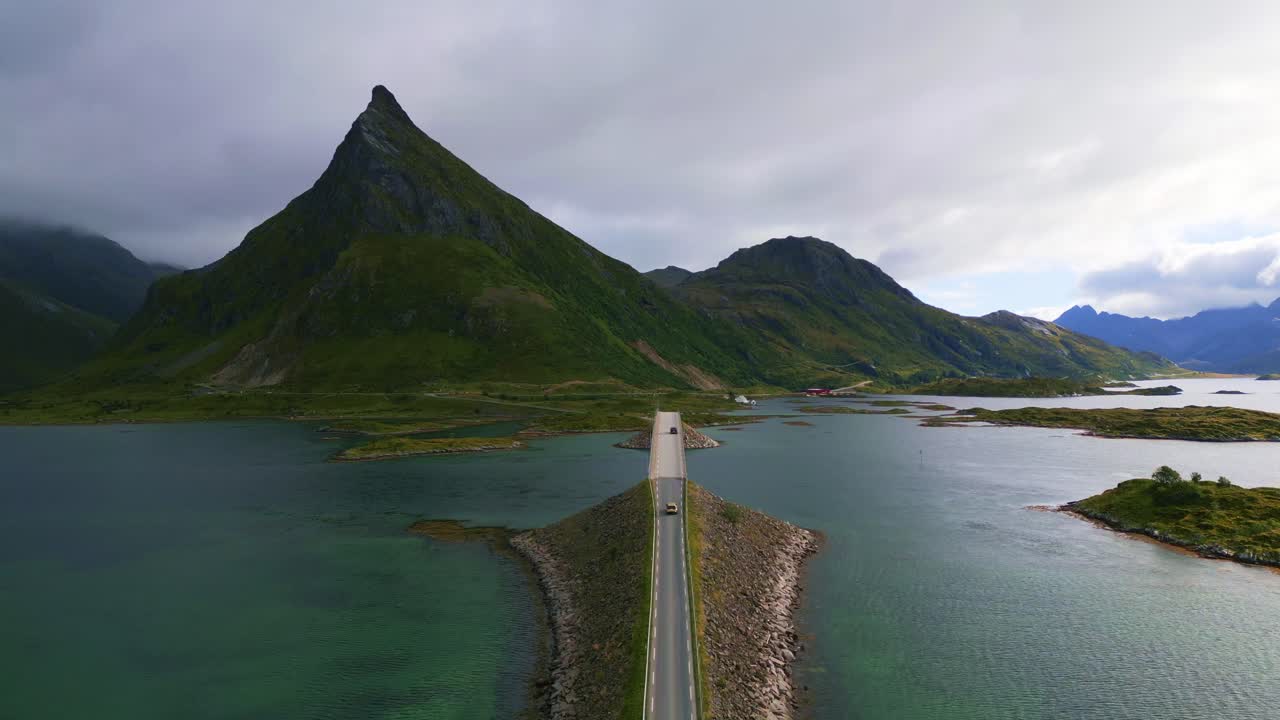Following cars driving along the Fredvang bridge in Lofoten Northern Norway with the sea ocean water shimmering in light turquoise blue and green tones in summer with view to the mountains