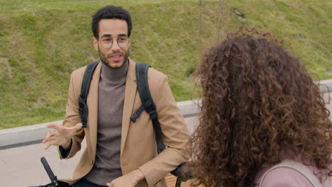 american man talking with his female friend while leaning on bike in the city