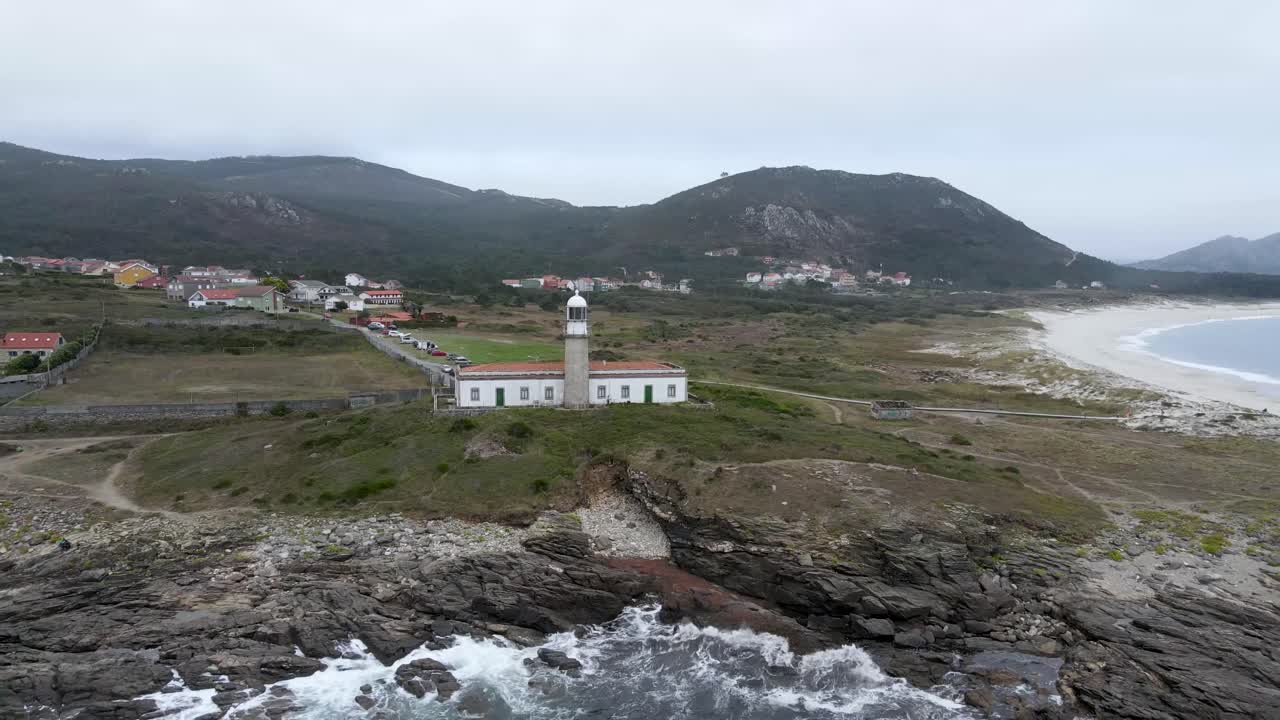 vista aérea en 4k del faro de punta lariño con un paisaje montañoso de fondo durante un día nublado