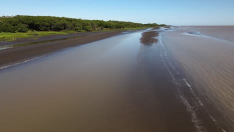 Aerial-pan-of-coast-of-Rio-de-la-Plata,-person-sits-in-chair-and-waves