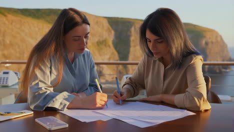 two women collaborating on design plans with a scenic ocean view