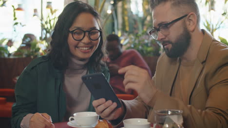 Cheerful-Multiethnic-Colleagues-Using-Smartphone-and-Chatting-in-Cafe