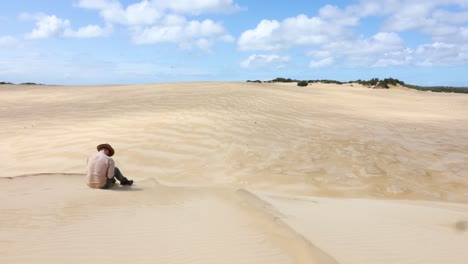 Un-Bosquimano-Australiano-Que-Lleva-Un-Akubra-Se-Sienta-Al-Borde-De-Dunas-De-Arena-épicas