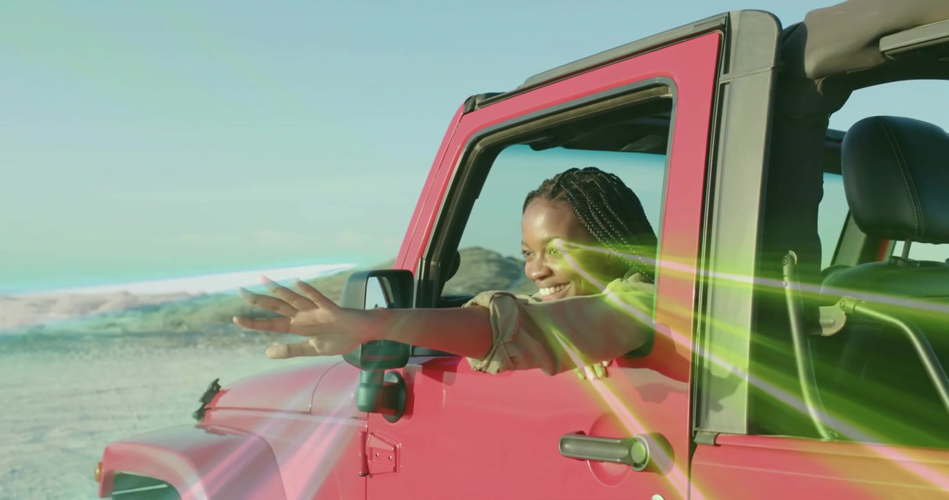 Jeep rossa da viaggio che guida lungo la spiaggia, mostrando un bagliore dell'obiettivo mentre una donna si sporge, si allunga e sente la brezza.
