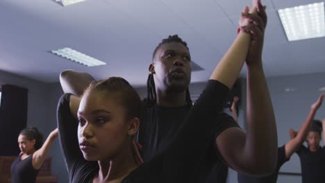 mixed race fit male modern dancer supporting female dancer while stretching up