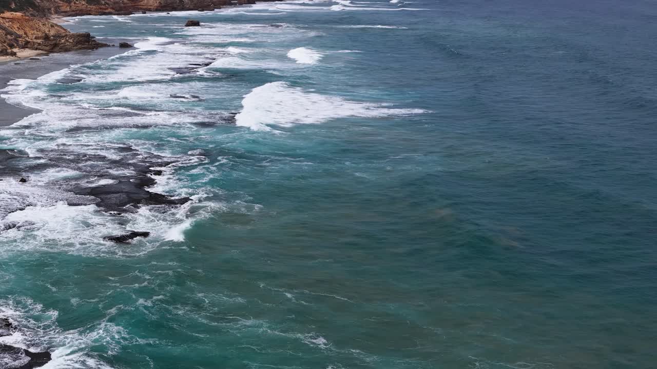 Drone captures turquoise waves crashing against rugged rocks under natural daylight along Sorrento coastline