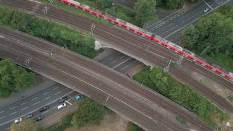 birds eye view of a railway bridge crossing a big street with a red commuter train crossing the bridge to the north