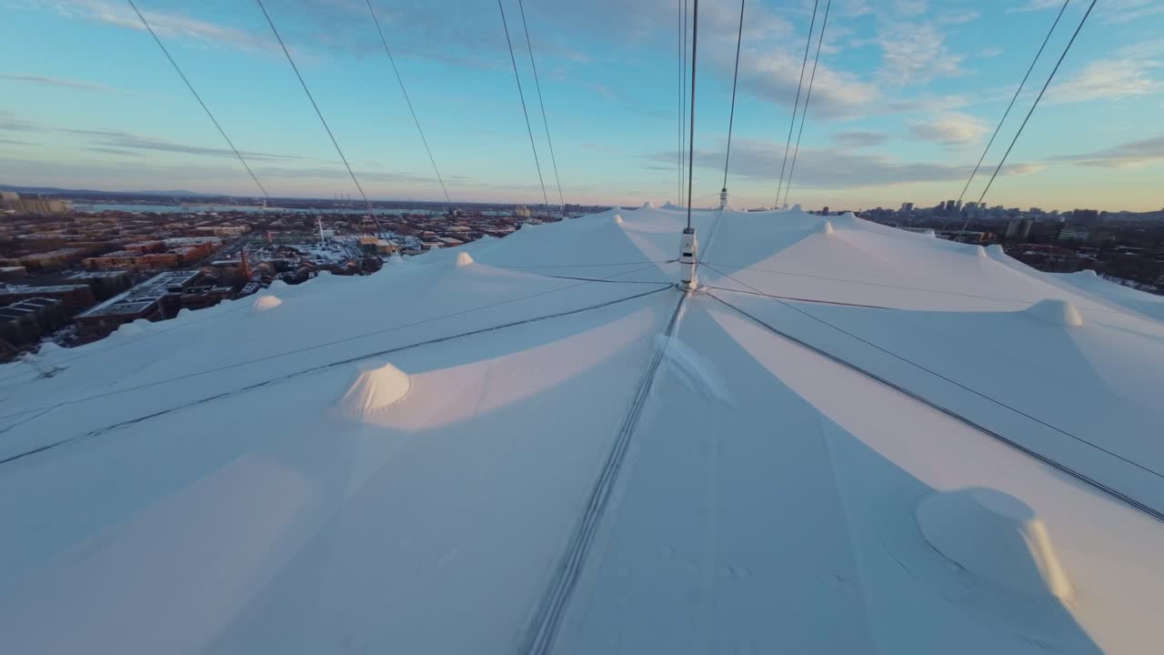 FPV drone swooping along snowy Olympic Stadium in Montreal, capturing dramatic winter sunset views