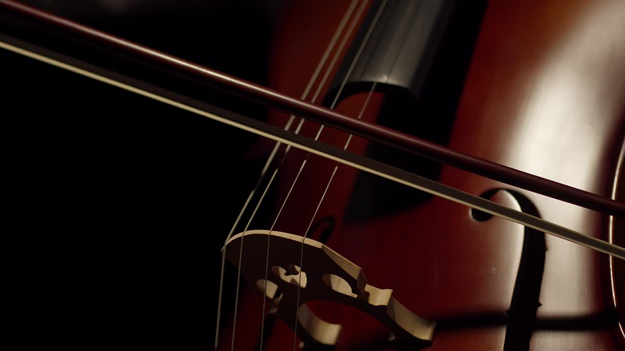 Artist plays with a bow on the strings of the cello in the darkness. Close-up musician plays with a bow of a violoncello