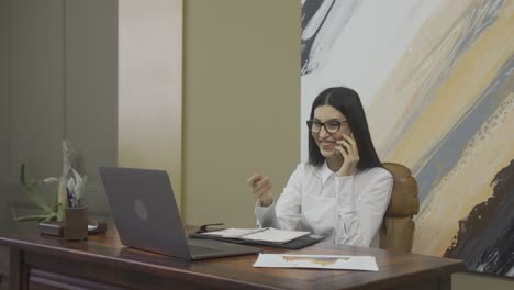 mujer de negocios caucásica hablando por teléfono móvil y escribiendo algo en la agenda mientras está sentada en el escritorio de la oficina