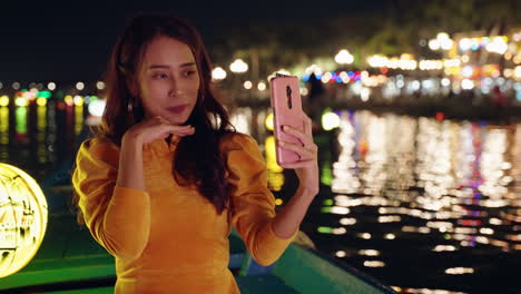 Junge-Frau-In-Einem-Gelben-Ao-Dai-Macht-Nachts-Ein-Selfie-Am-Fluss-In-Hoi-An