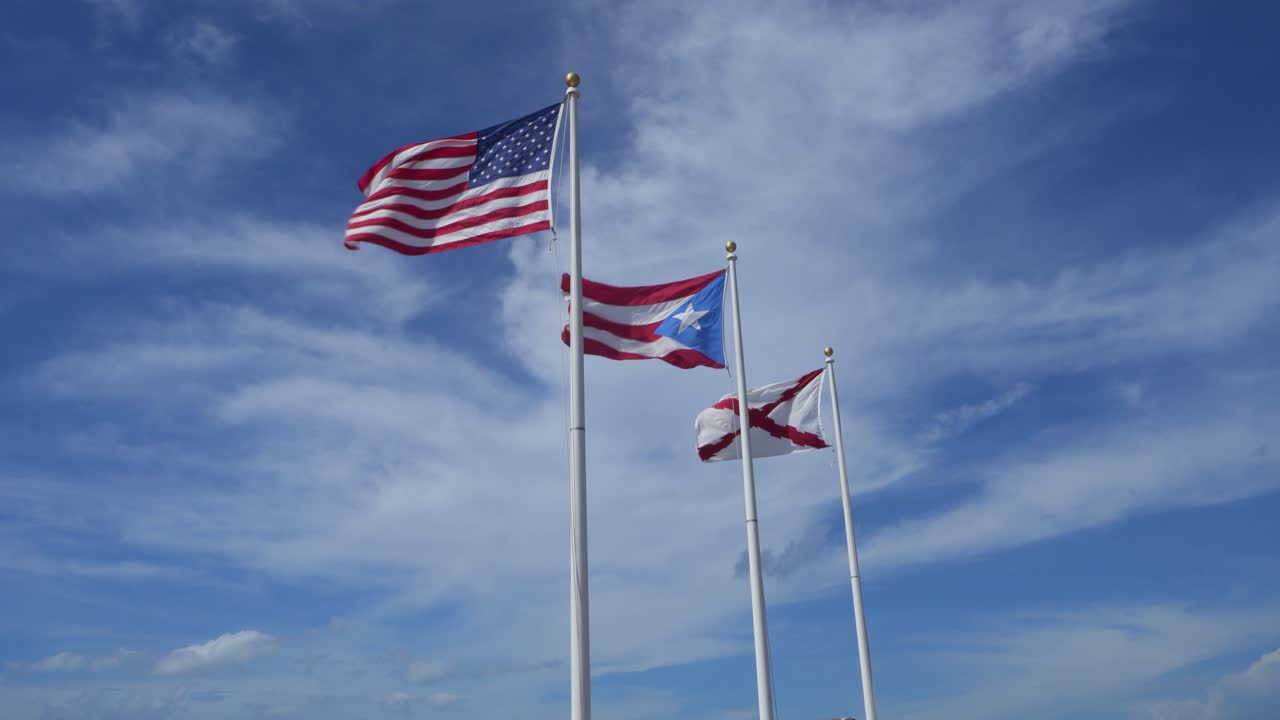 Flags on flag poles flying against blue sky in Puerto Rico, American and burgundy.