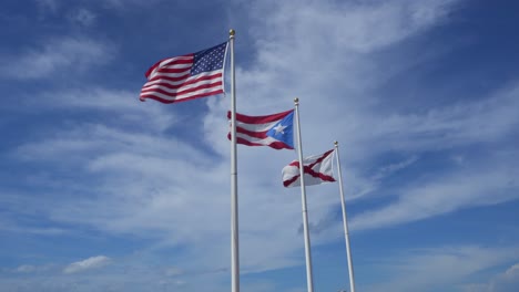flags on flag poles flying against blue sky in puerto rico, american and burgundy.