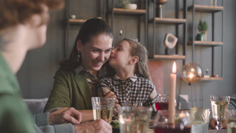 Kleines-Mädchen-Flüstert-Mama-Ein-Geheimnis-Ins-Ohr,-Während-Es-Während-Eines-Familienessens-Am-Tisch-Sitzt