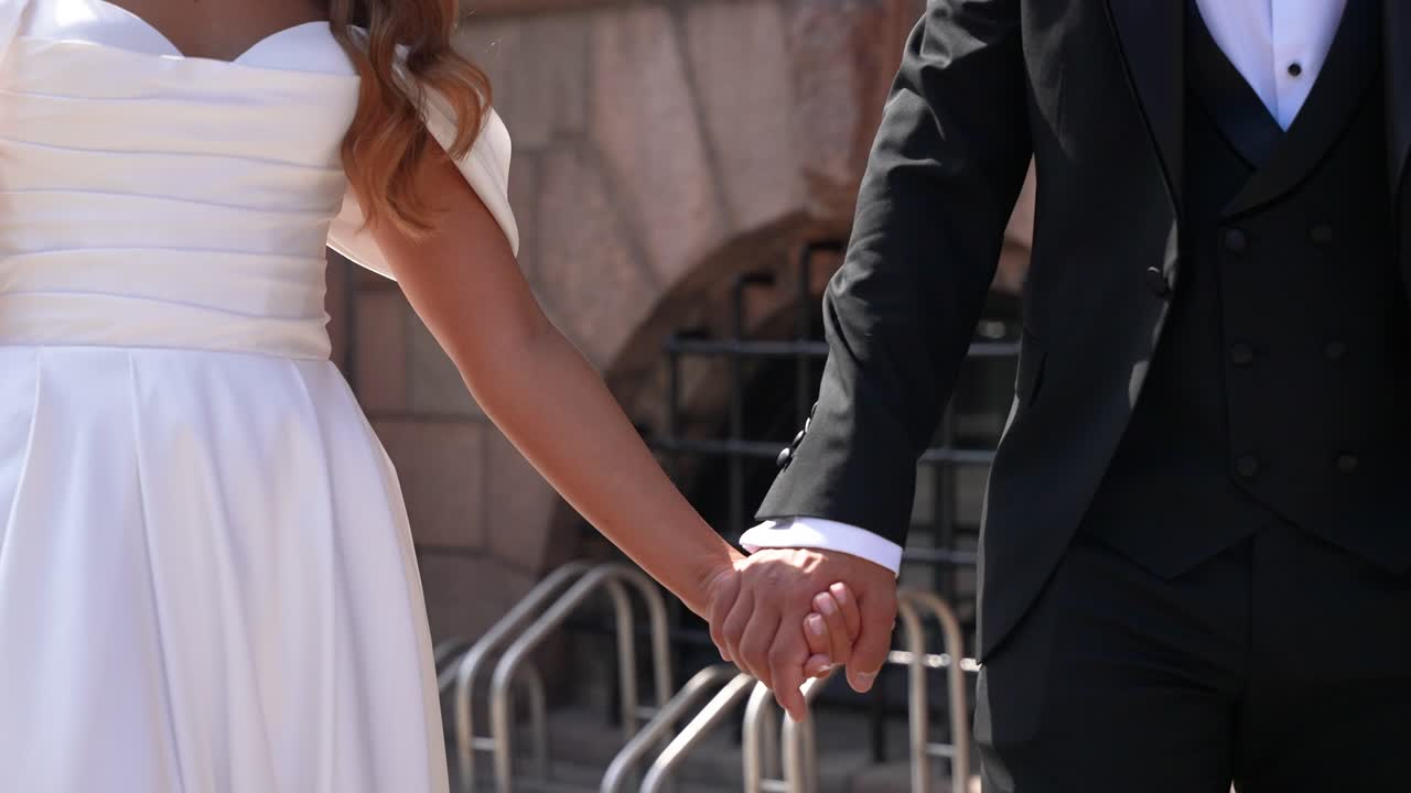 Questa intima inquadratura ravvicinata cattura le mani di una sposa e uno sposo mentre camminano insieme gioiosamente dopo la cerimonia. L'illuminazione mette in risalto il legame emotivo e l'eleganza del momento.