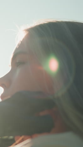 dama blanca con guantes negros inclina la cabeza hacia atrás, ajustando su cabello con la luz del sol creando un efecto brillante alrededor de su cara, suavemente borrosa vegetación en el fondo