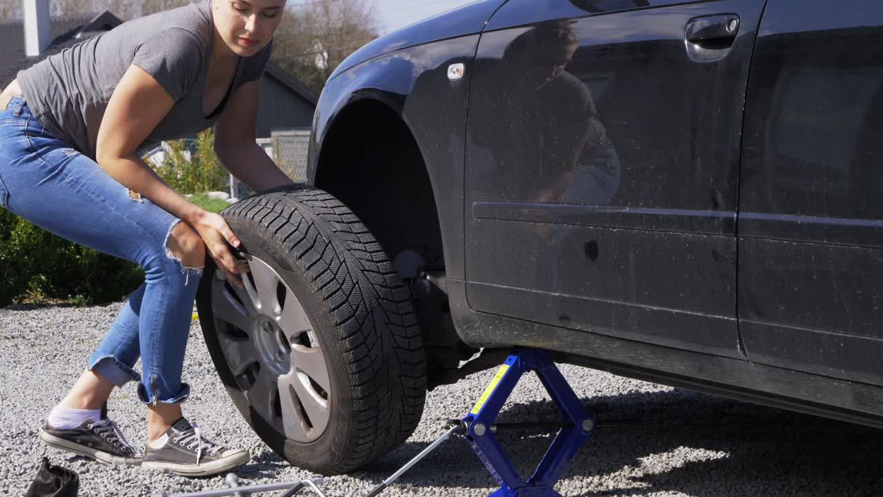 joven mujer casual cambiando neumático de coche desinflado al lado de la carretera