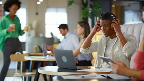 businessman wearing wireless headphones working on laptop in informal seating area of modern office