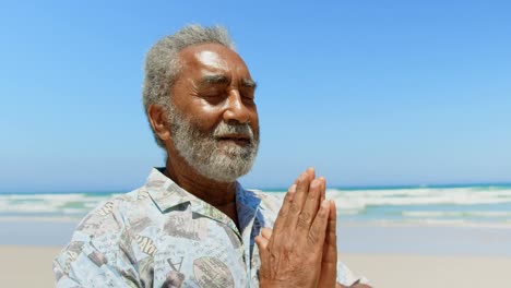 front view of active senior african american man performing yoga on the beach 4k