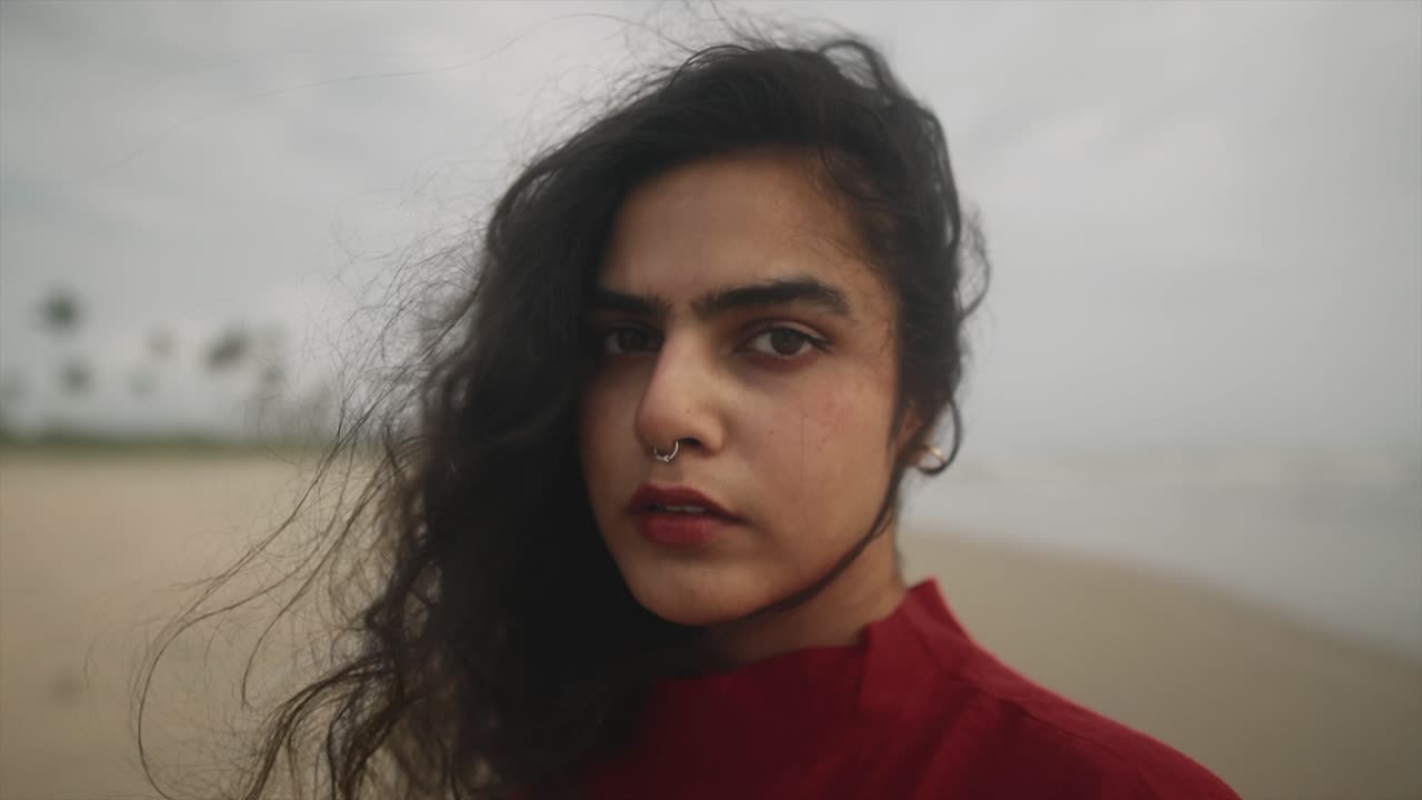toma cinematográfica de una modelo de moda india con un vestido rojo en una playa de arena en goa, india en un día ventoso y sosteniendo un globo rojo en su mano