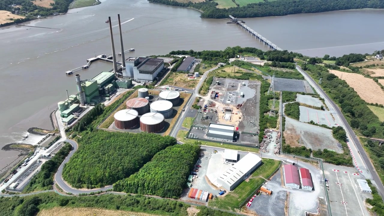 Drone orbit. Elevated drone perspective of electricity infrastructure on the River Suir, County Wexford. Sustainable energy facility surrounded by natural Irish landscapes and peaceful river scenery.