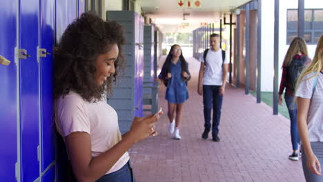 girl using phone and boy using locker in school corridor