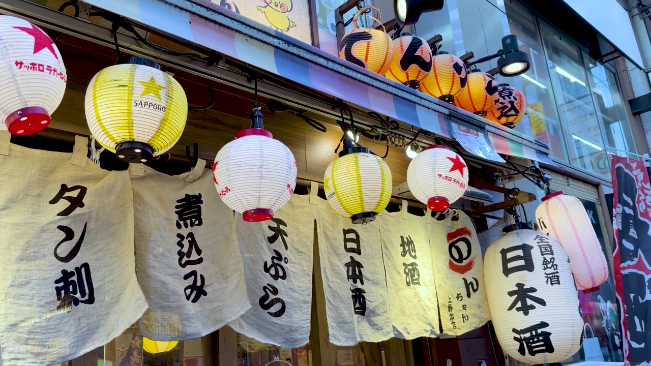 Inquadratura dal basso di lanterne di carta illuminate e tende di tessuto all'esterno di un ristorante di Tokyo.