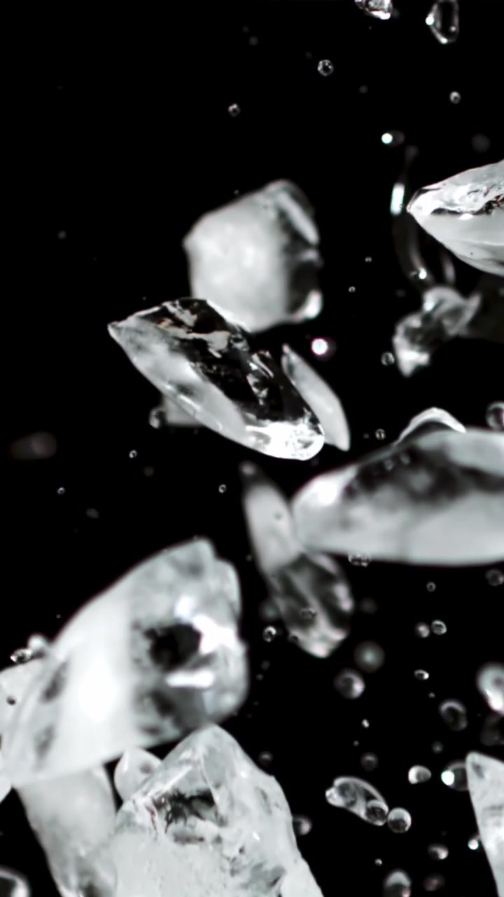 Cubetti di ghiaccio e goccioline d'acqua che salgono al rallentatore su sfondo nero