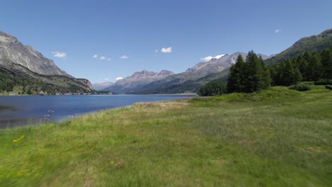 Toma-Cinematográfica-Aérea-De-Un-Prado-Verde-Junto-A-Un-Río-Y-Algunas-Montañas-En-El-Horizonte-En-Silvaplana,-Suiza