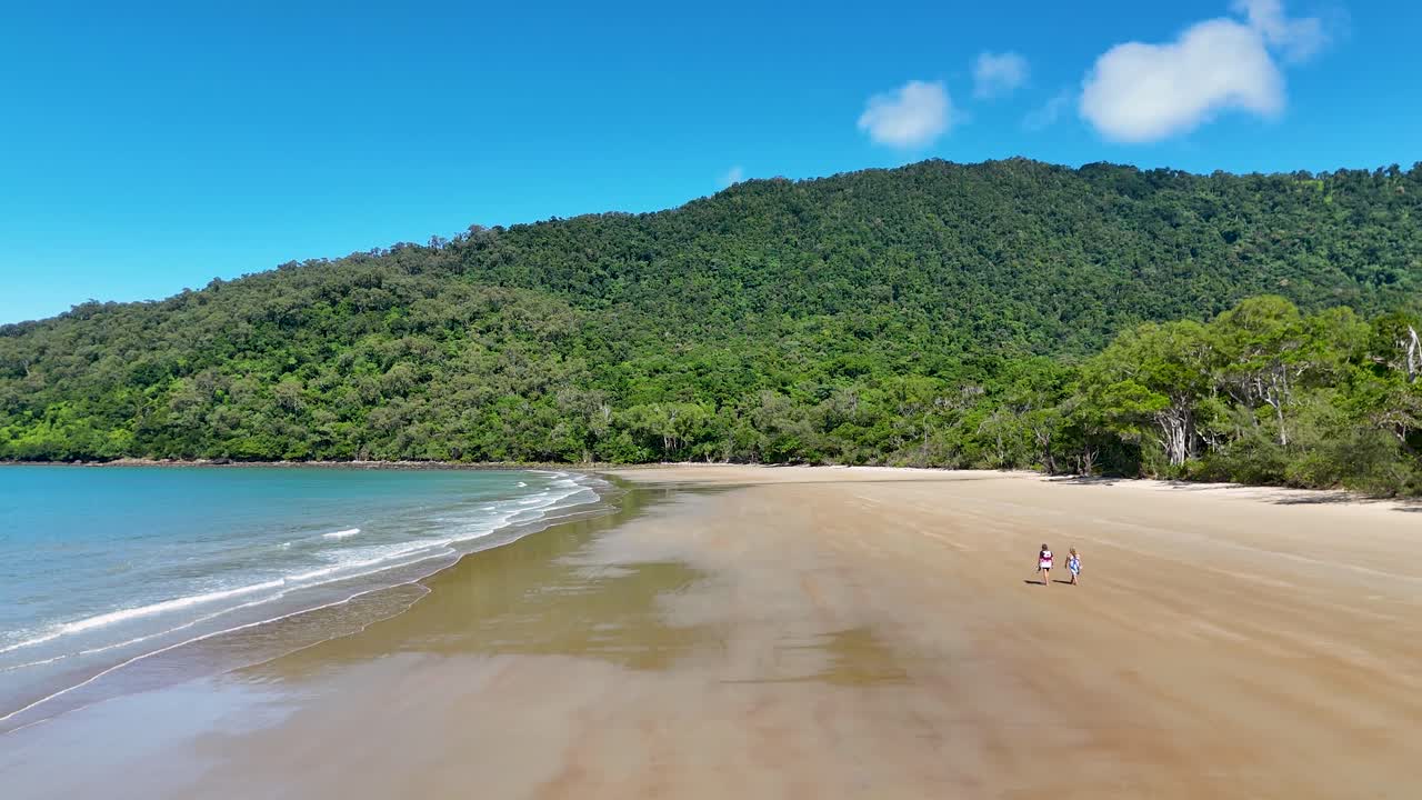 Aerial view of a couple walking along a pristine, isolated beach in Port Douglas, surrounded by lush greenery and clear skies