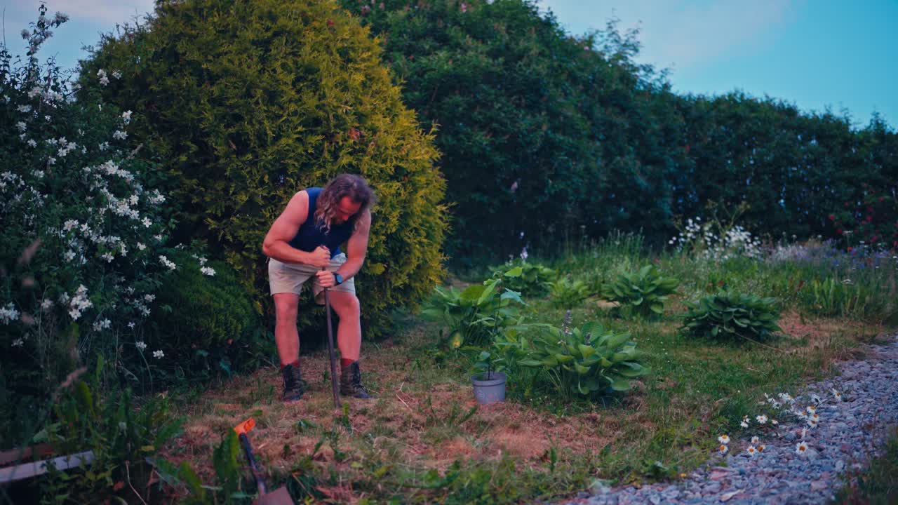 Um homem usa uma barra de escavação para quebrar e soltar o solo, preparando o terreno para o plantio - Plano Estático.