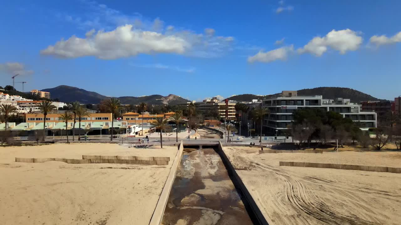 Enjoy a tranquil vista of Santa Ponsa beach in Mallorca, featuring golden sand, a gentle stream, and swaying palm trees under a bright blue sky. Perfect for relaxation and nature lovers.