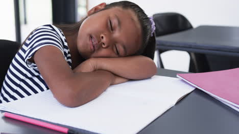 in a school classroom, a young biracial girl is asleep at her desk