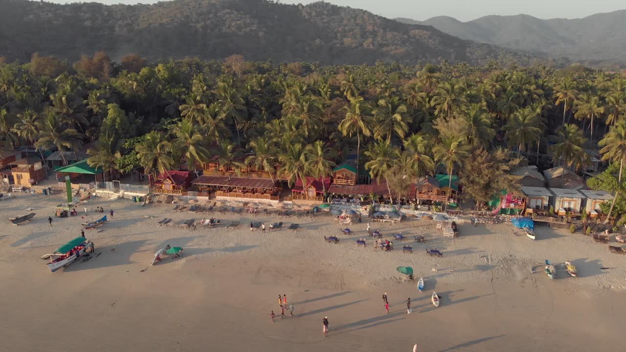 Riprese aeree in 4K con drone che panoramicano una spiaggia al tramonto a Palolem, India, affollata di visitatori da tutto il mondo.