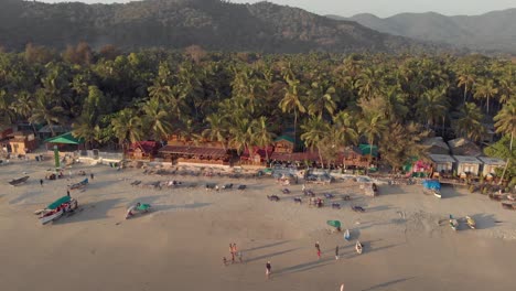 Imágenes-Aéreas-De-Drones-De-4k-Que-Recorren-Una-Playa-Al-Atardecer-En-Palolem,-India,-Llena-De-Visitantes-De-Todo-El-Mundo