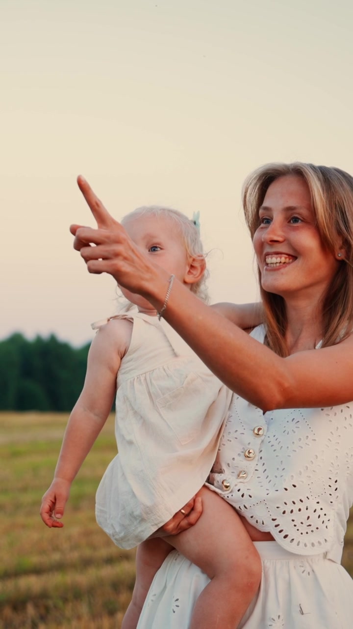 Giovane madre che tiene in braccio la sua bambina piccola in un campo al tramonto