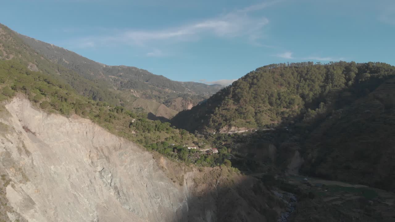 deslizamiento de roca gigante en la ladera de una montaña tallada por el río a continuación, las casas y las tierras de cultivo se ven en la distancia en el valle montañoso mientras se invierte la revelación aérea