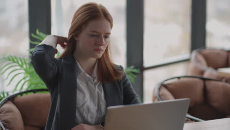 thoughtful concerned redheaded woman working on laptop computer looking away thinking solving problem at office serious woman search for inspiration make decision feel lack of ideas