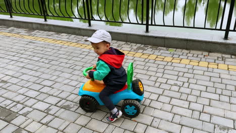 lovely little kid riding his toy car pushing from the floor. child rides along the artificial pond.