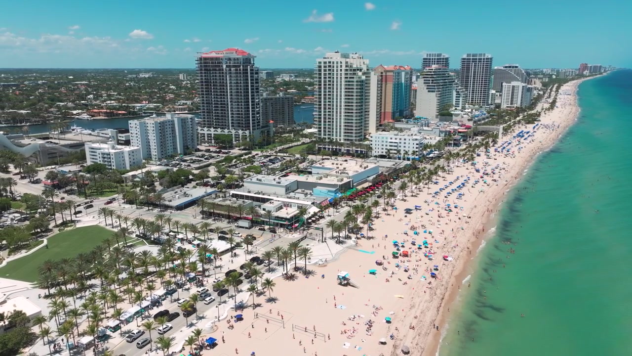 Vista aérea a gran altura de Fort Lauderdale, Florida — la "Venecia de América" — que muestra bañistas, palmeras, yates y el animado horizonte urbano costero.