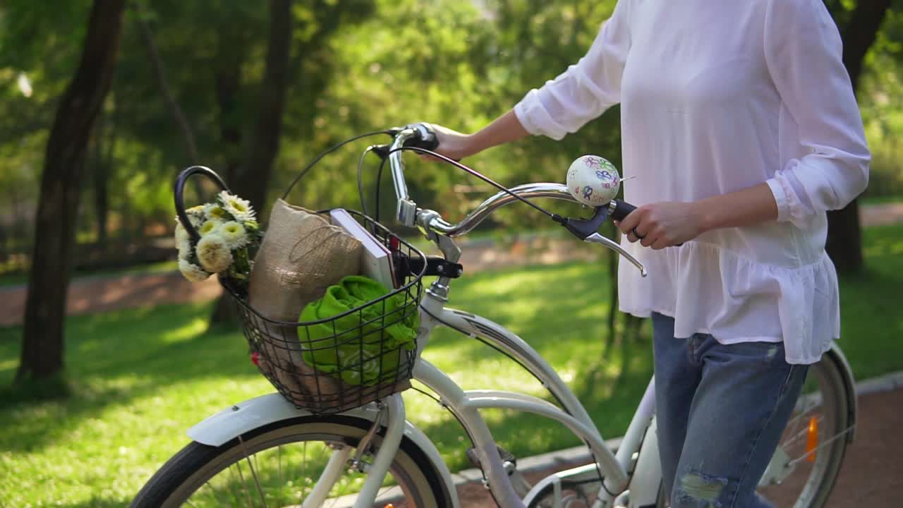 Close Up view of woman's hands holding a handlebar of a city bicycle with a basket with flowers and book. Woman enjoying her time