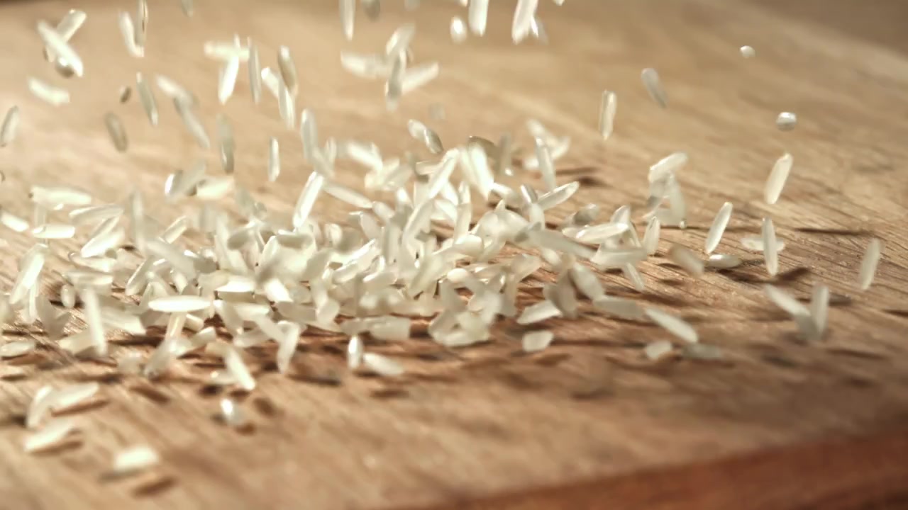 Primo piano di chicchi di riso crudo che cadono su una tavola di legno.