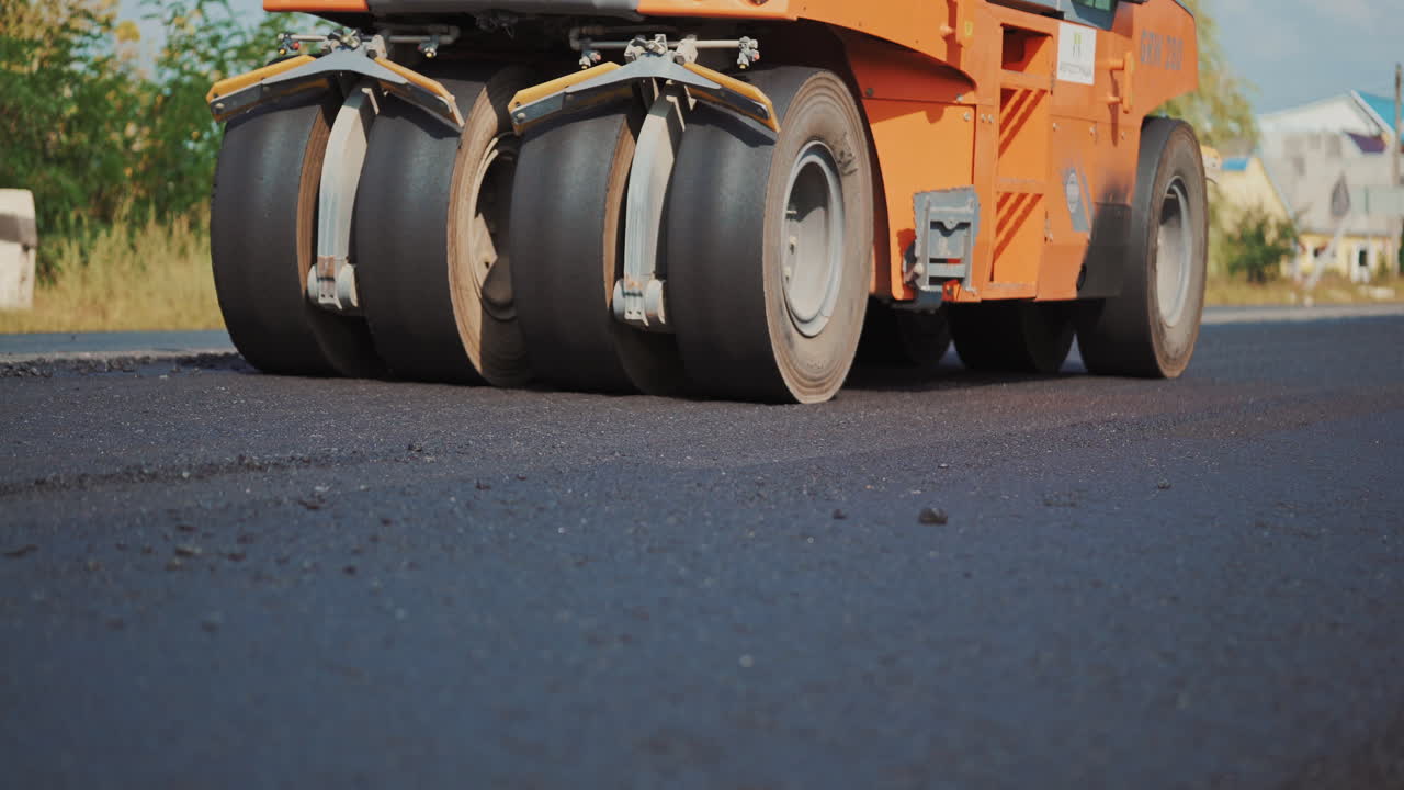 Modern asphalt roller machine stuck and press hot asphalt while making a new road. Big black wheels of a roller machine working on the new road.
